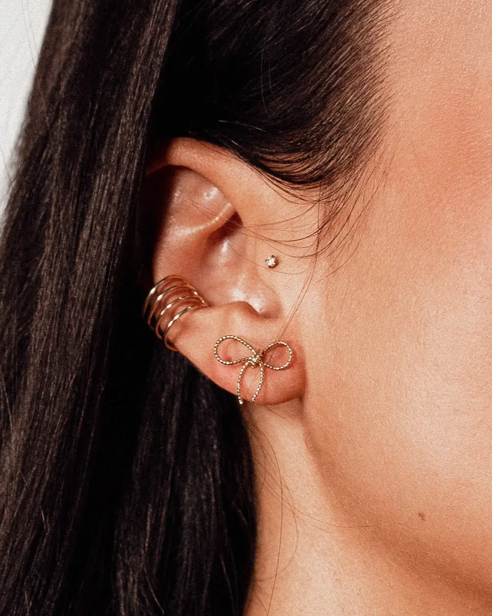Model wearing IGGI Jewellery Bow Stud Earrings in 18k gold-filled finish – delicate bow design styled with multiple ear piercings.