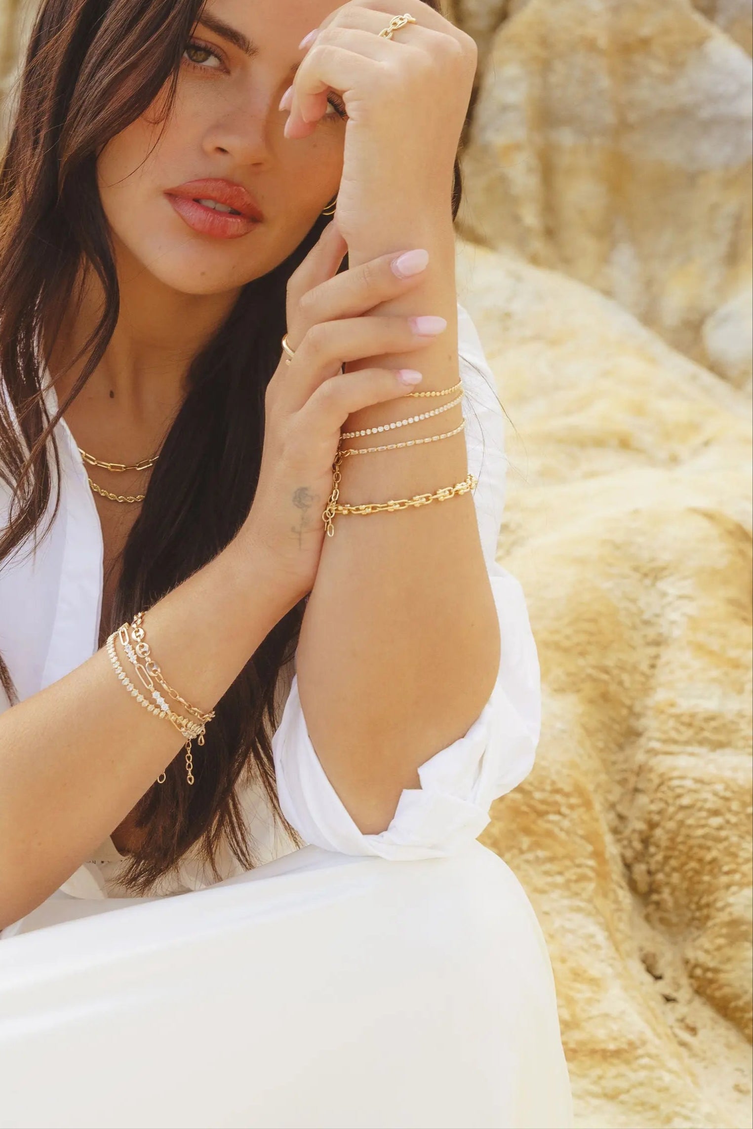 Model wearing IGGI Jewellery chunky link chain bracelet styled with layered gold chains, sitting against a rocky backdrop.