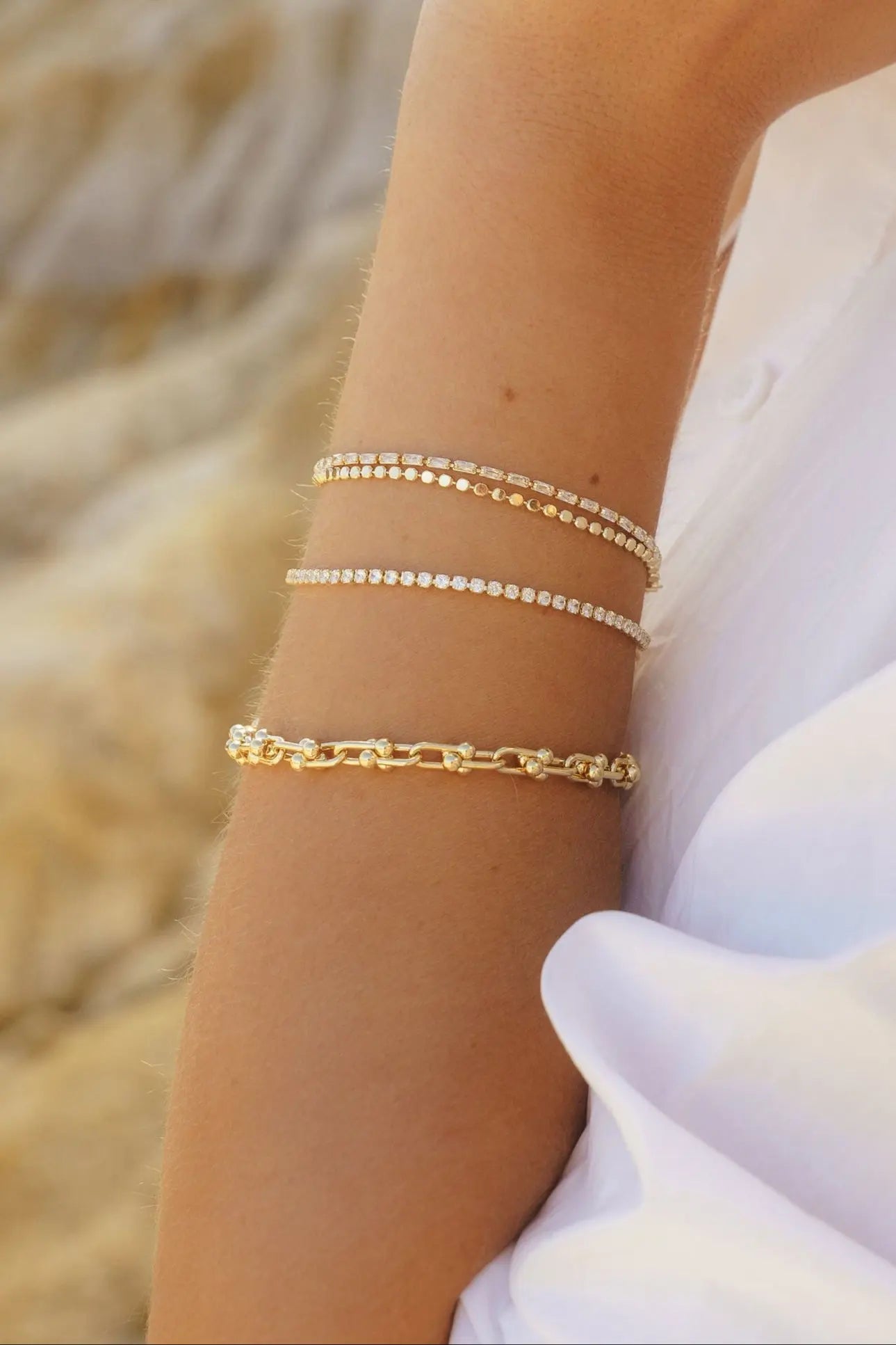 Close-up of IGGI Jewellery chunky link chain bracelet stacked with delicate gold chains on wrist.
