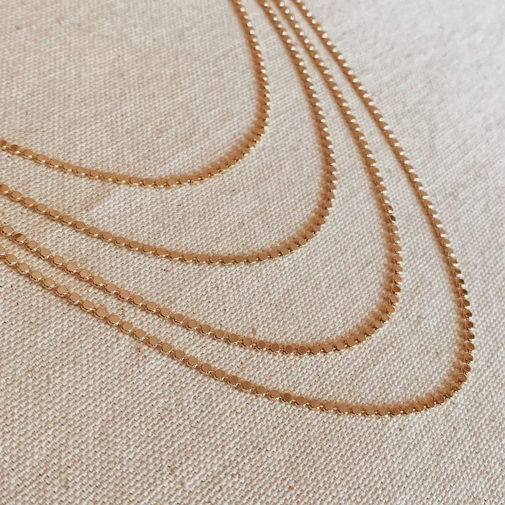 Flat lay of layered Dotted Chain Necklaces in 18k gold-filled, styled on neutral fabric background