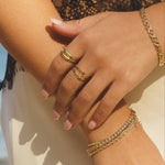 Close-up of model wearing Gwen Ring in 18k gold-filled on hand, styled with layered gold bracelets and rings in natural light