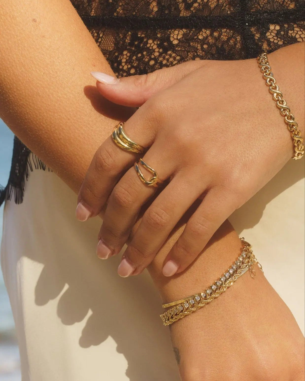 Close-up of model wearing Gwen Ring in 18k gold-filled on hand, styled with layered gold bracelets and rings in natural light