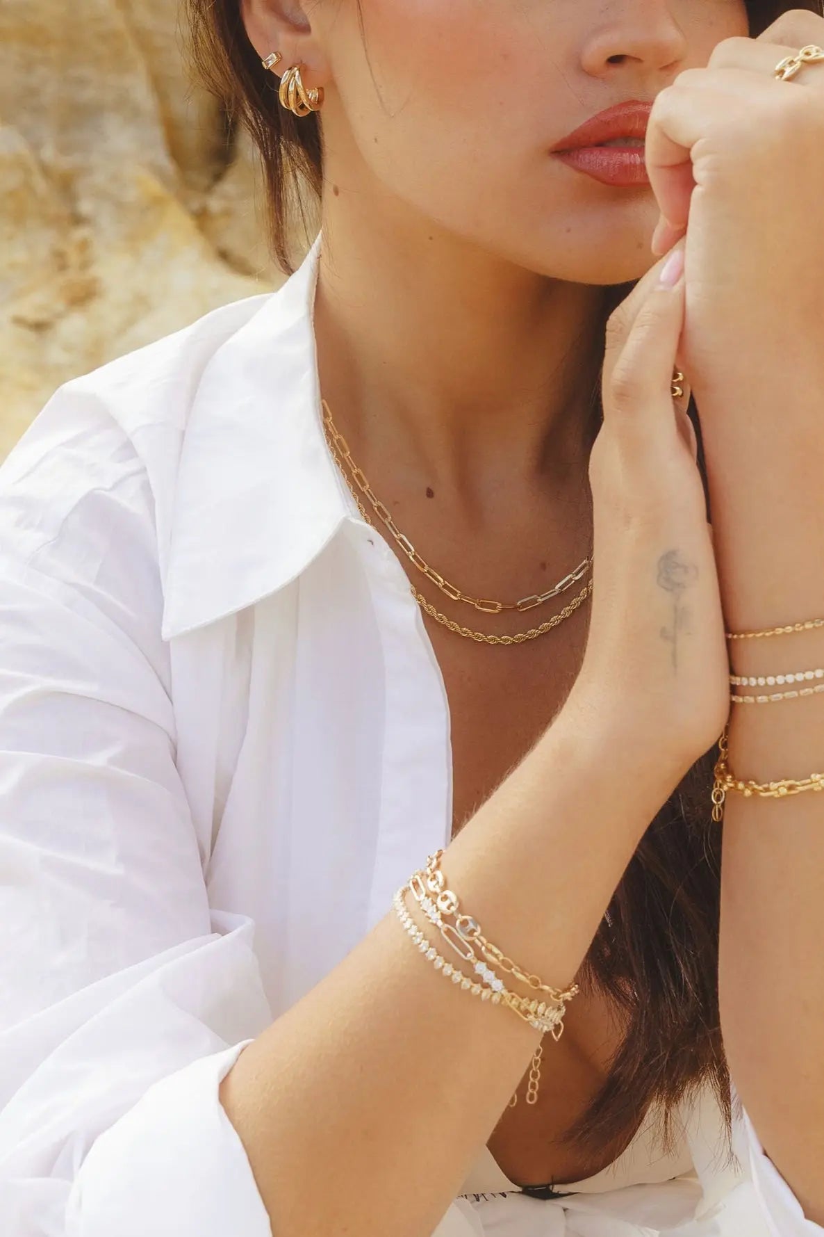 Model wearing 18k gold-filled paperclip chain necklace layered with IGGI bracelets and rings – outdoor editorial