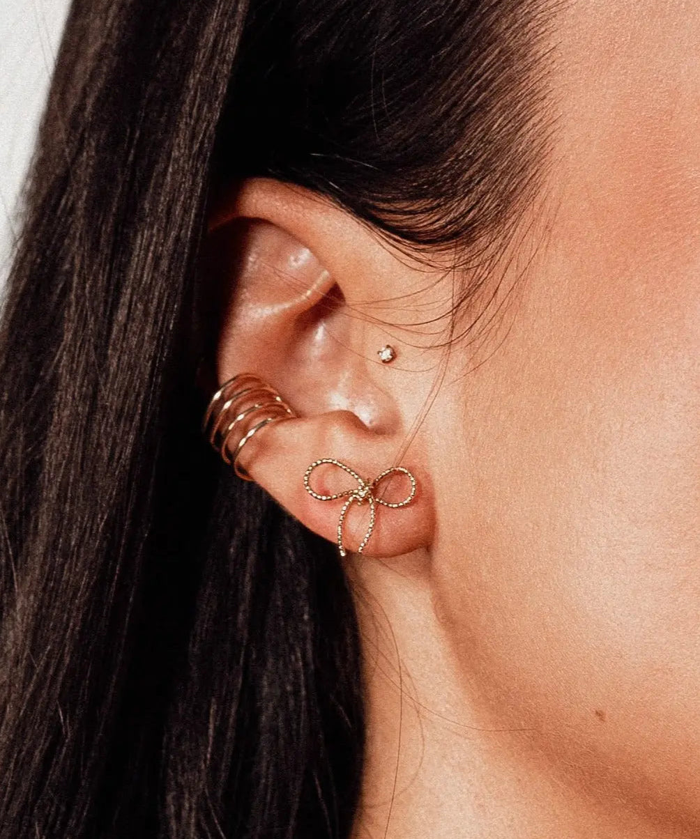 Model wearing IGGI Jewellery Bow Stud Earrings in 18k gold-filled finish – delicate bow design styled with multiple ear piercings.