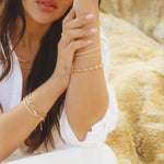 Model wearing IGGI Jewellery chunky link chain bracelet styled with layered gold chains, sitting against a rocky backdrop.