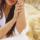 Model wearing IGGI Jewellery chunky link chain bracelet styled with layered gold chains, sitting against a rocky backdrop.