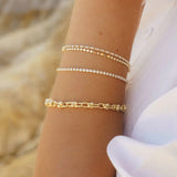 Close-up of IGGI Jewellery chunky link chain bracelet stacked with delicate gold chains on wrist.