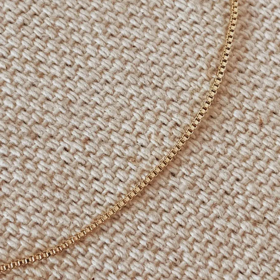 Dainty Box Chain Bracelet laid flat on woven fabric, showcasing box-style links