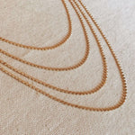 Flat lay of layered Dotted Chain Necklaces in 18k gold-filled, styled on neutral fabric background