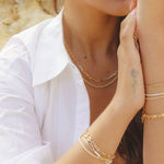 Model wearing 18k gold-filled paperclip chain necklace layered with IGGI bracelets and rings – outdoor editorial
