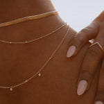 Close-up of IGGI Jewellery Star Drop Necklace in 18k gold-filled, layered with gold chains and styled on model’s neckline in warm natural light