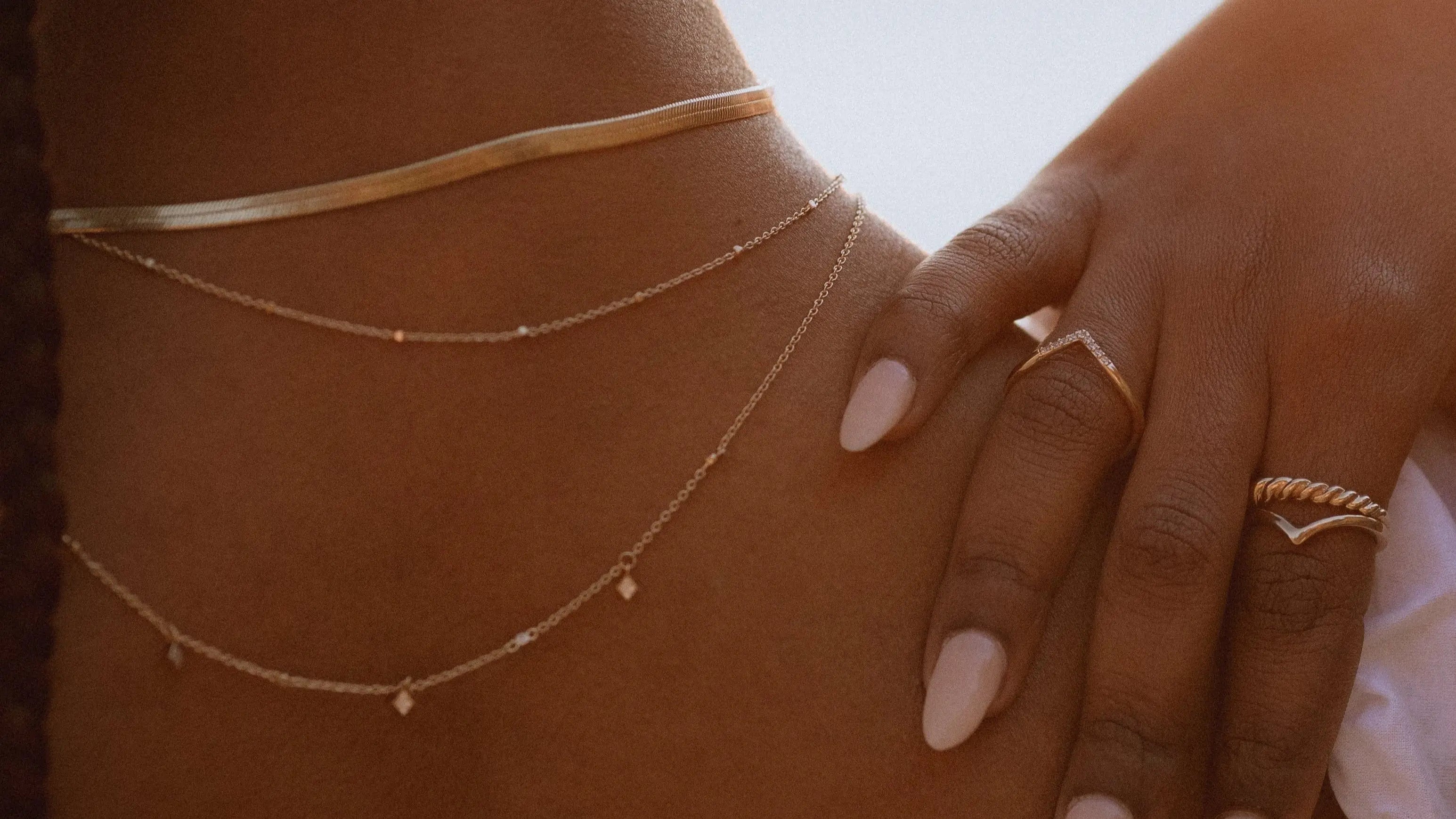 Close-up of IGGI Jewellery Star Drop Necklace in 18k gold-filled, layered with gold chains and styled on model’s neckline in warm natural light