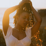 Model wearing IGGI Jewellery Star Drop Necklace in 18k gold-filled, layered with gold chains, photographed during golden hour with a warm sunset glow